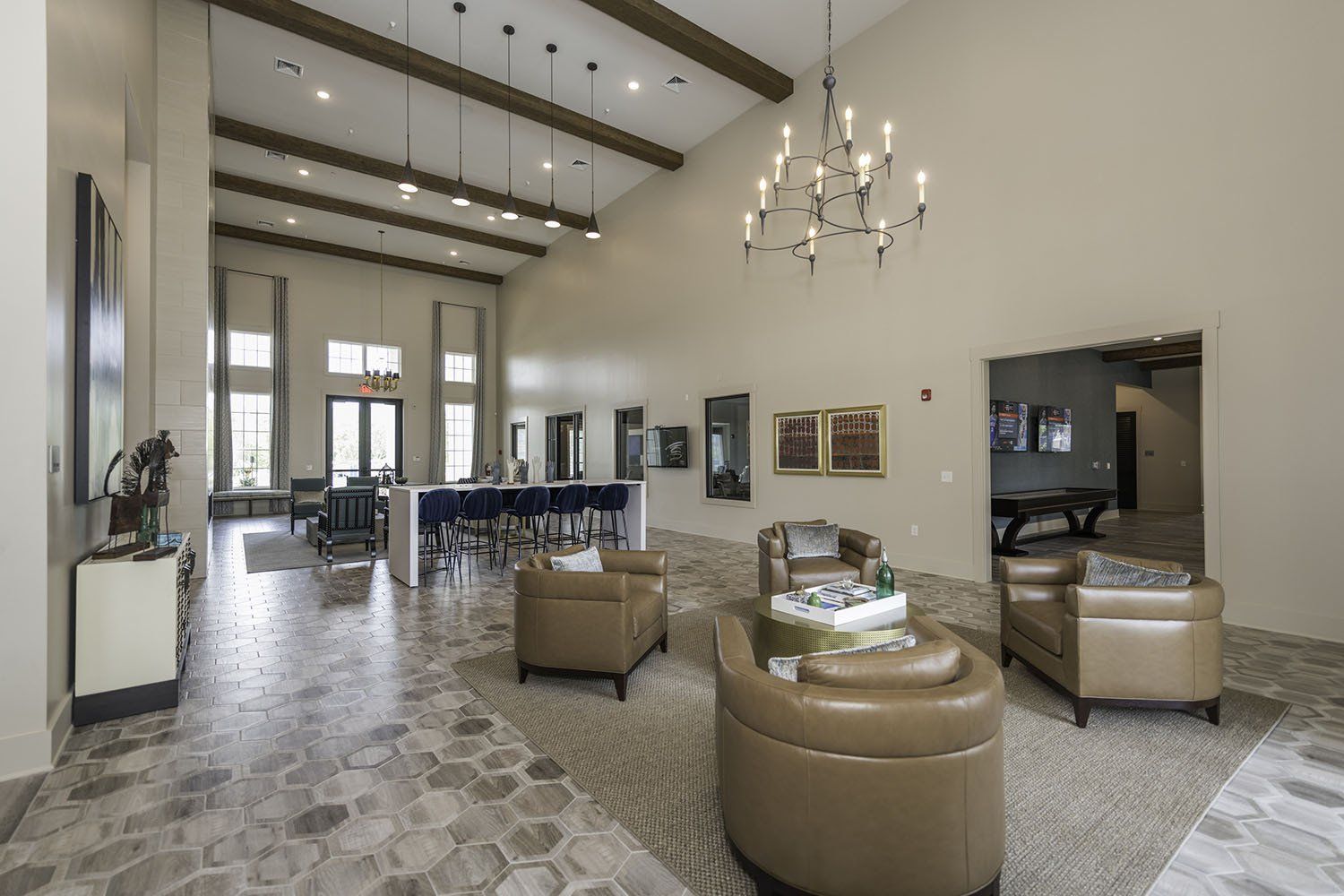 A spacious, high-ceilinged clubhouse interior with tan armchairs, a central dining counter, and decorative chandeliers at Silver Collection at Carl D. Silver Parkway in Fredericksburg, VA..