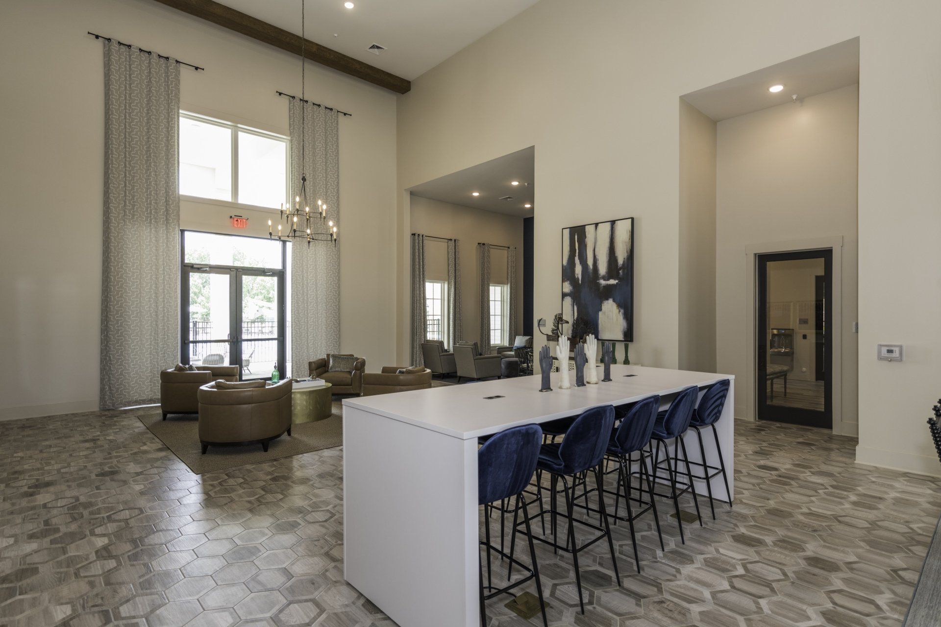 A tall, modern lobby with tile floors, a long white table with blue stools, and a seating area near a tall window at Silver Collection at Carl D. Silver Parkway in Fredericksburg, VA..