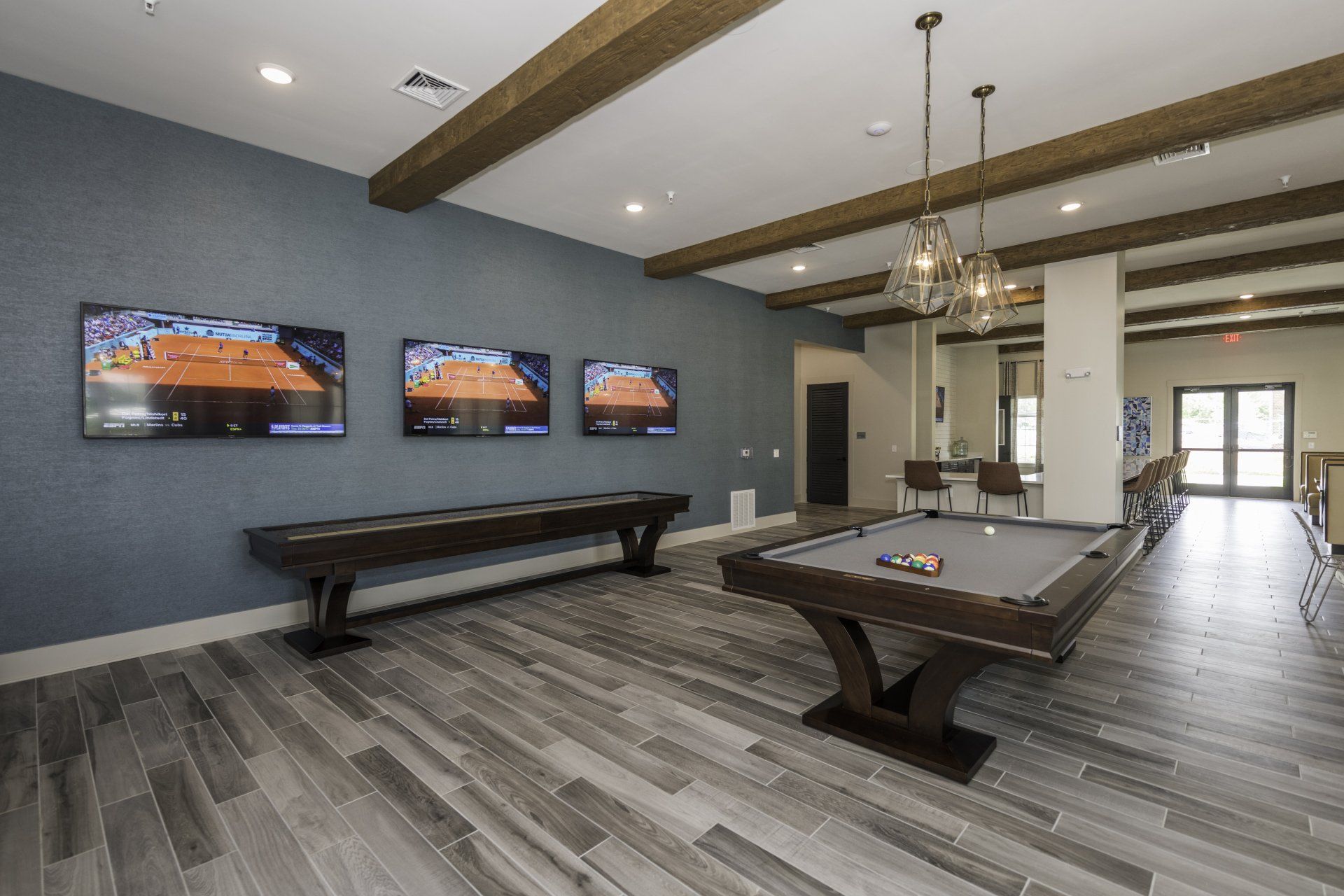 A game room with a pool table, a shuffleboard table, three wall-mounted TVs, and gray wood-look flooring at Silver Collection at Carl D. Silver Parkway in Fredericksburg, VA..