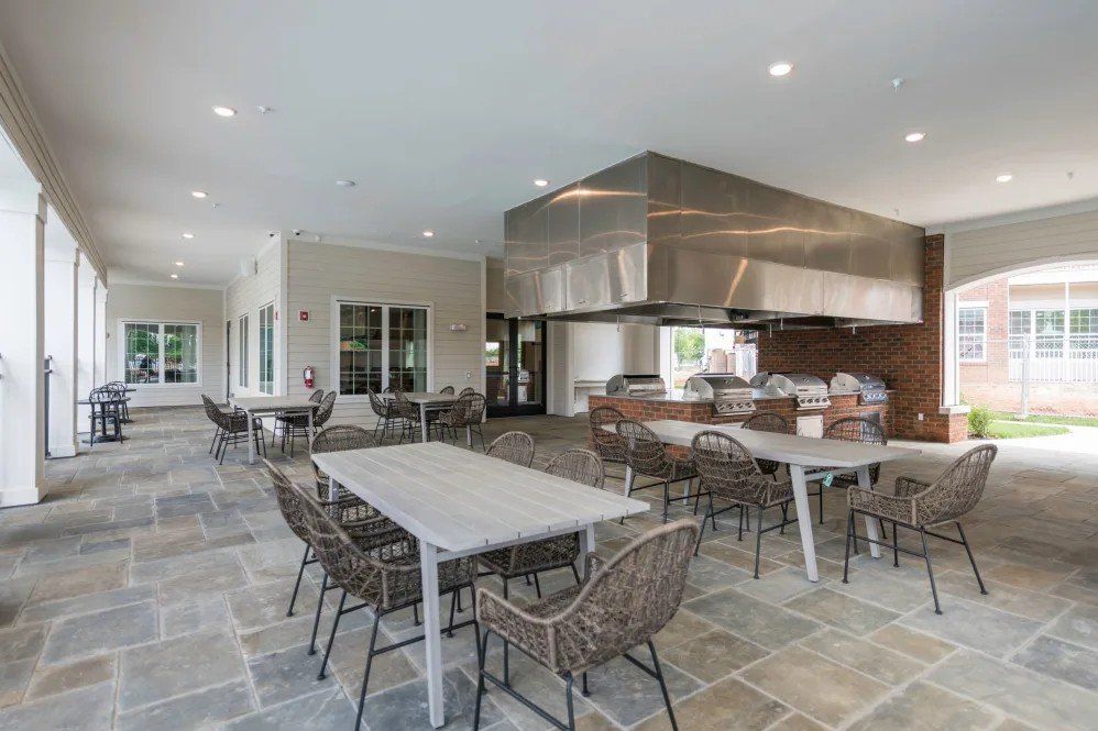 Outdoor dining area with stone flooring, tables, chairs, and a large stainless steel hood above grills.