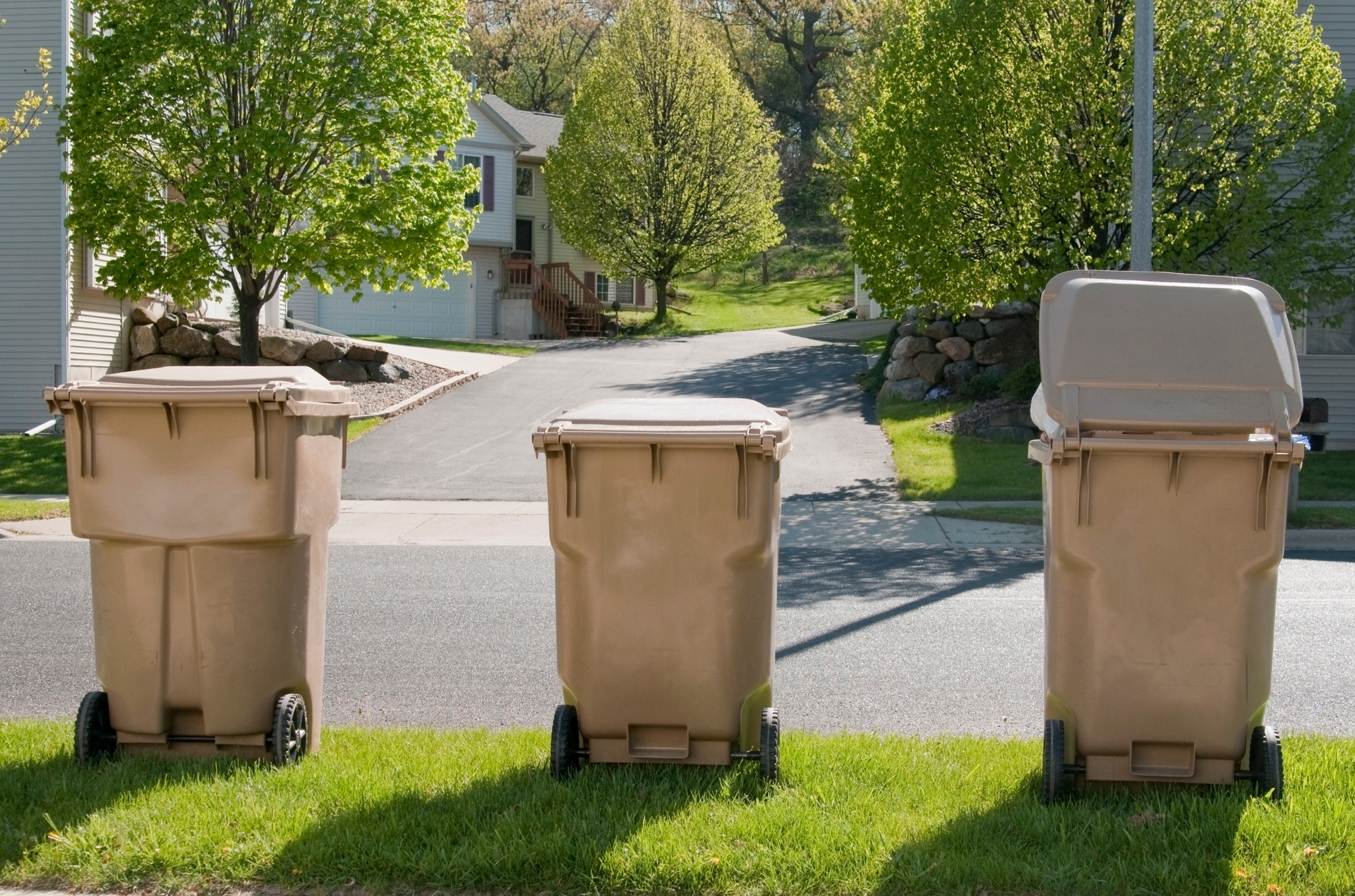 A blue dumpster is sitting in the grass in front of a house.