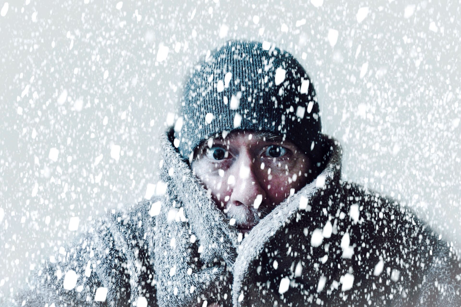 A man wearing a hat and scarf is standing in the snow.