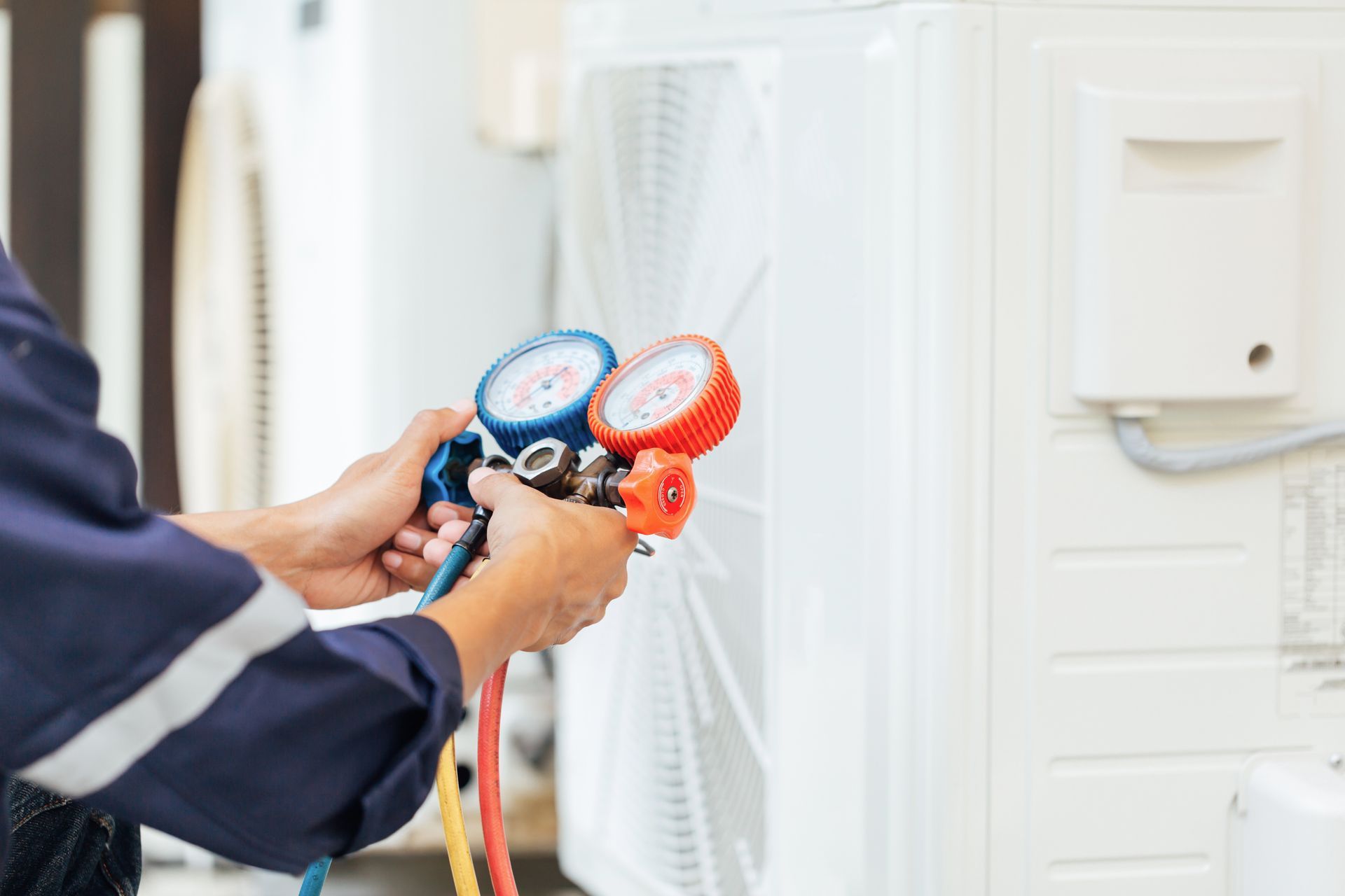 Technician using pressure gauges to service an outdoor air conditioning unit.