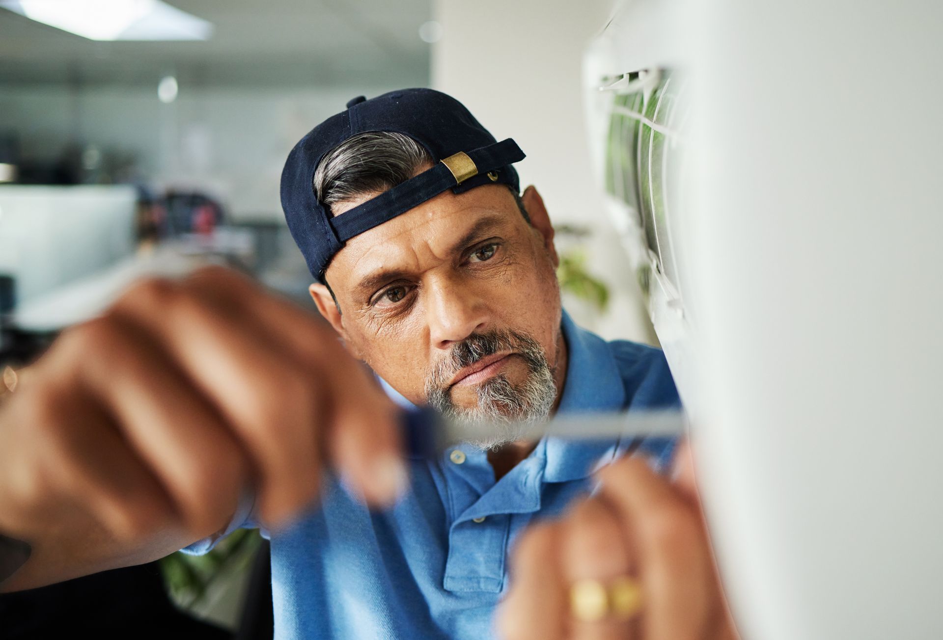 A technician wearing a blue shirt and cap working on wiring inside an electrical panel.