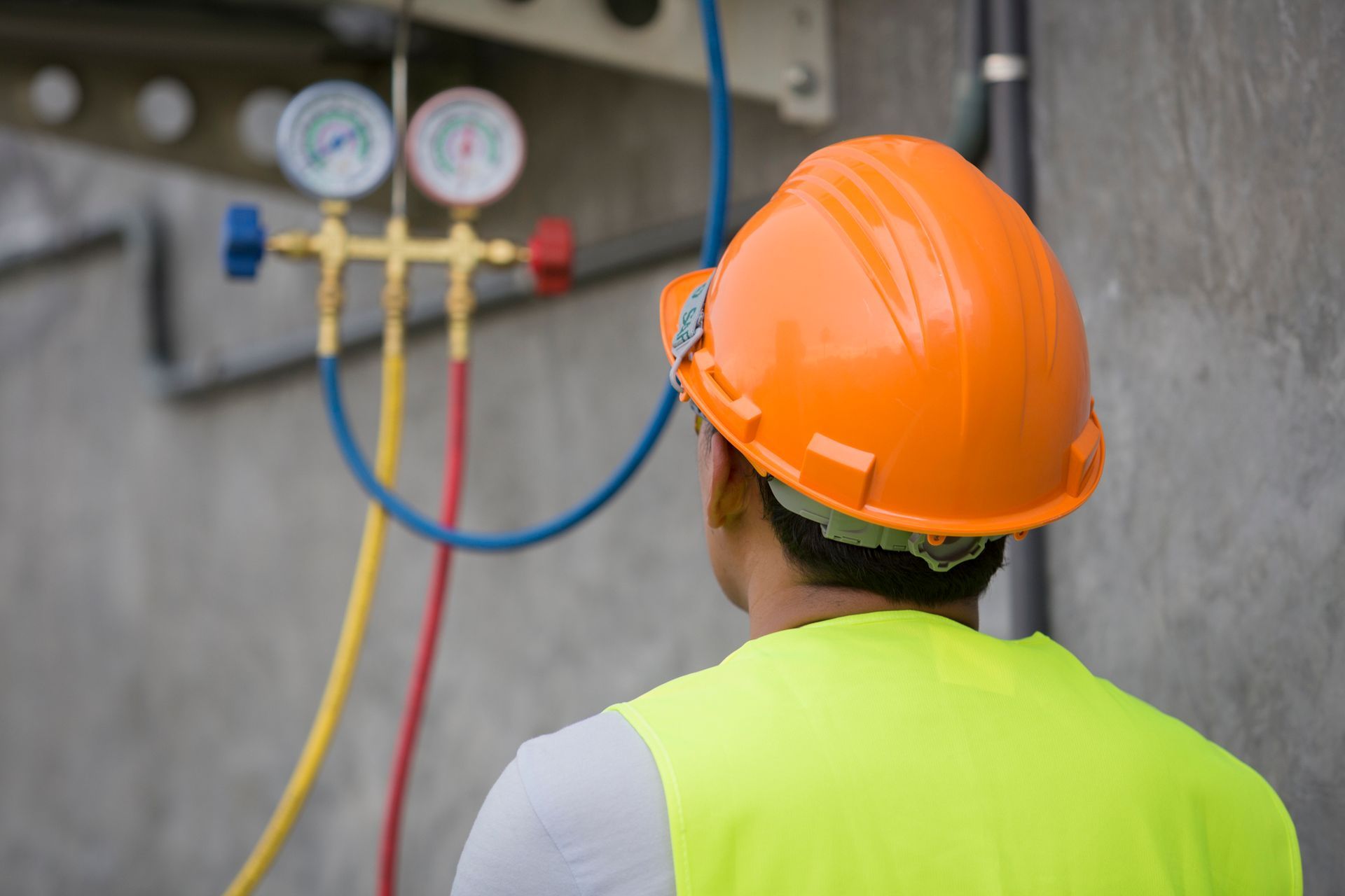 HVAC technician inspecting industrial gauges wearing safety gear on commercial equipment site.