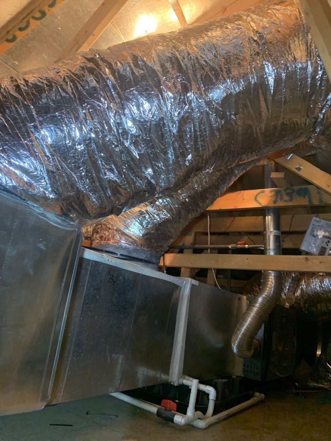 HVAC system in an attic. Ductwork connects to a metal box, with insulation. Wooden beams are visible.