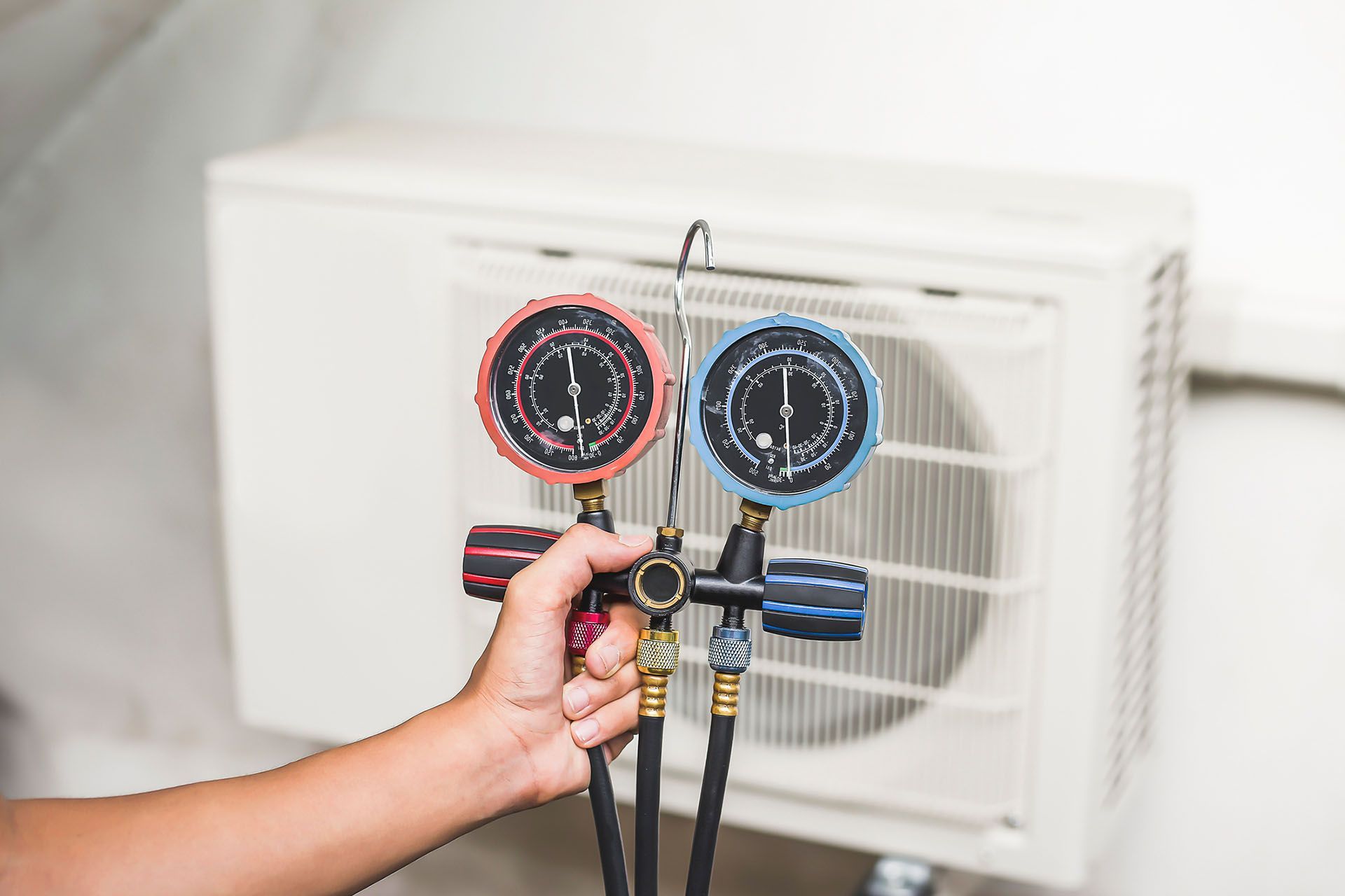 Technician using HVAC manifold gauges to test air conditioner pressure during maintenance service. Technician using HVAC manifold gauges to test air conditioner pressure during maintenance service.