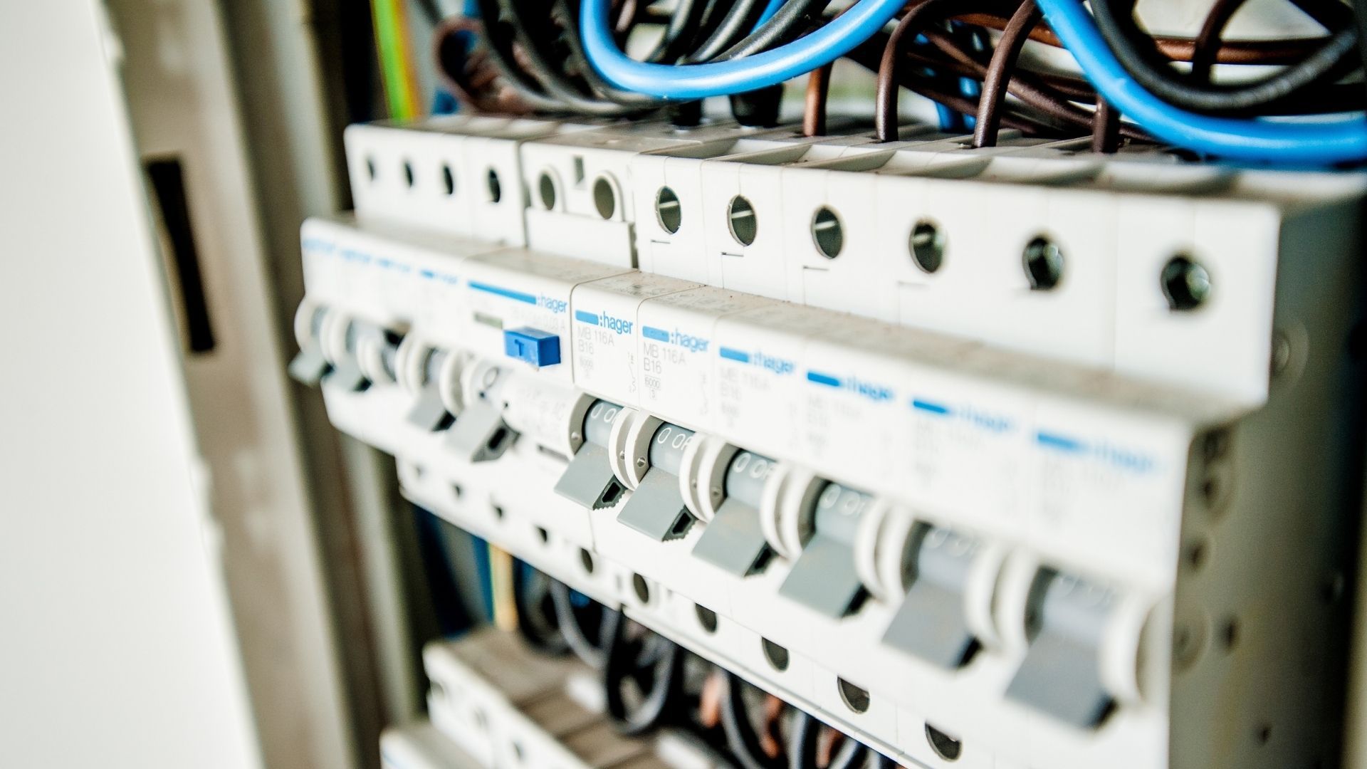 Person using a multimeter to test electrical wiring in a panel.