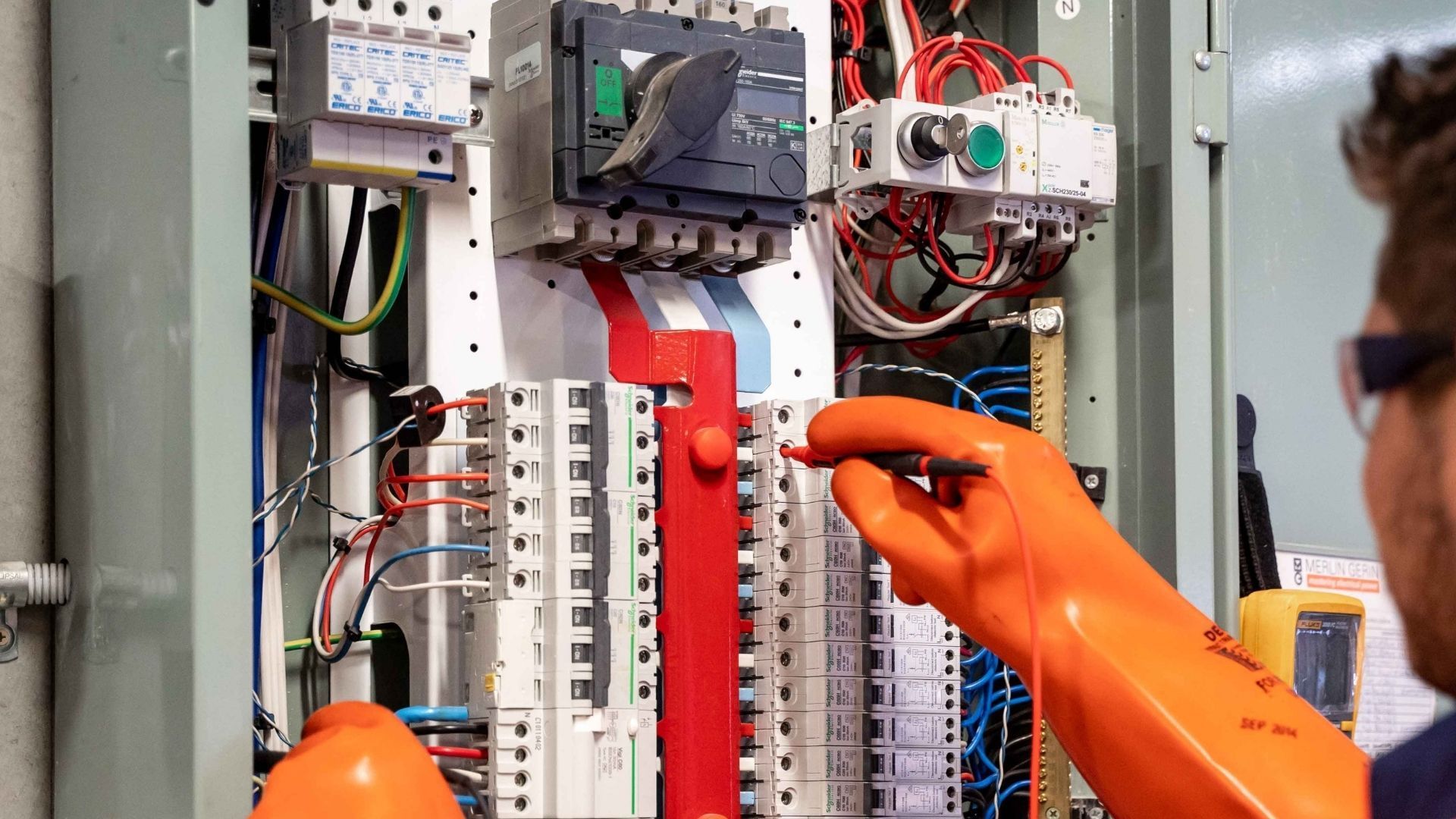 Person using a multimeter to test electrical wiring in a panel.
