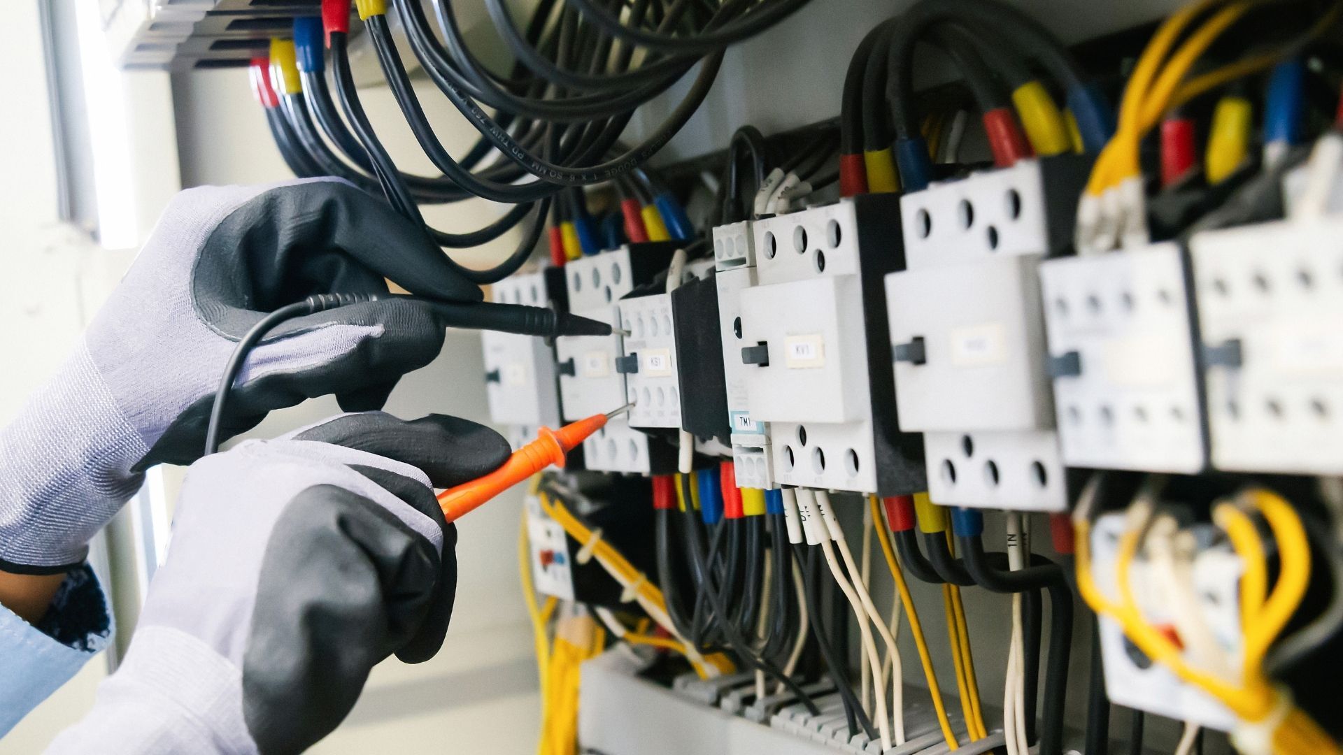 Person using a multimeter to test electrical wiring in a panel.