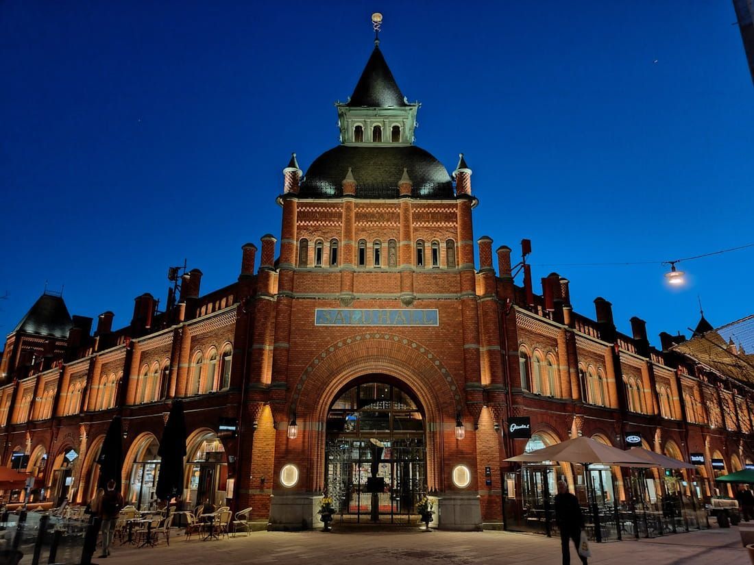 Historic red-brick market hall at dusk, with lit entrances and a blue evening sky