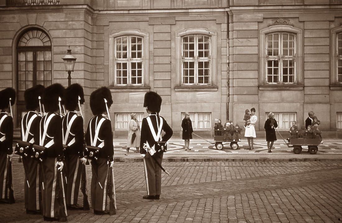 Soldiers in ceremonial uniforms stand in formation outside a historic stone building.