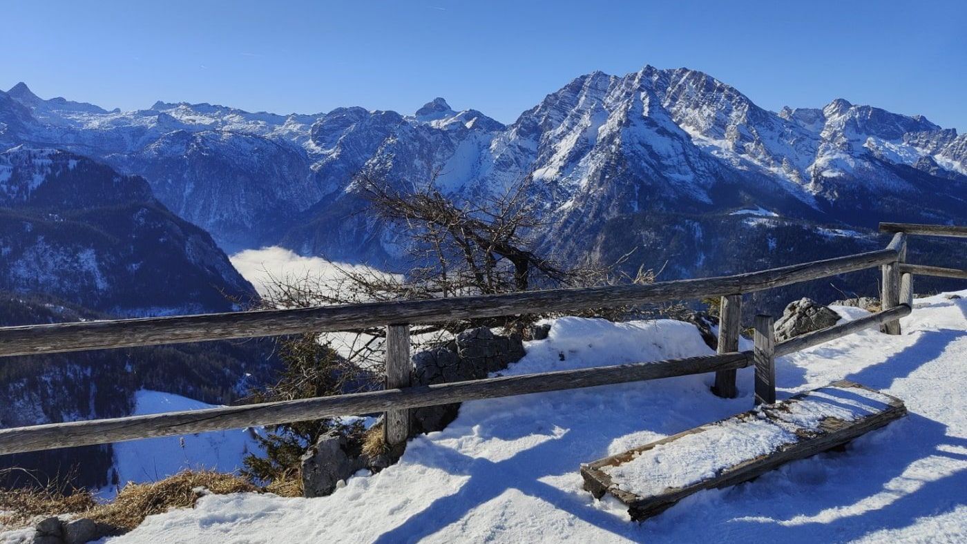 Königsblick A snowy mountain range with a wooden fence in the foreground
