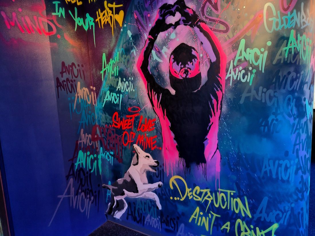 Graffiti-covered wall with a glowing pink-black figure and a white animal crouching below at night.