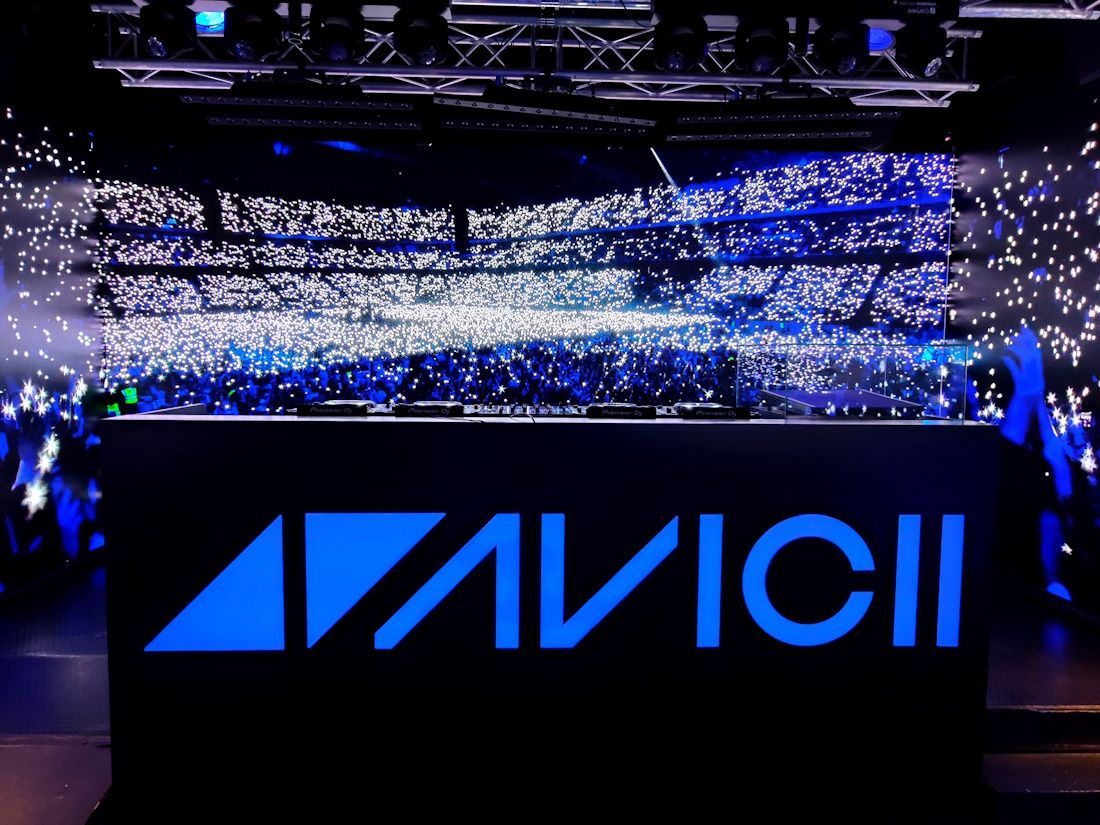 AVICII stage with blue lights and a crowd holding glowing phones in an arena