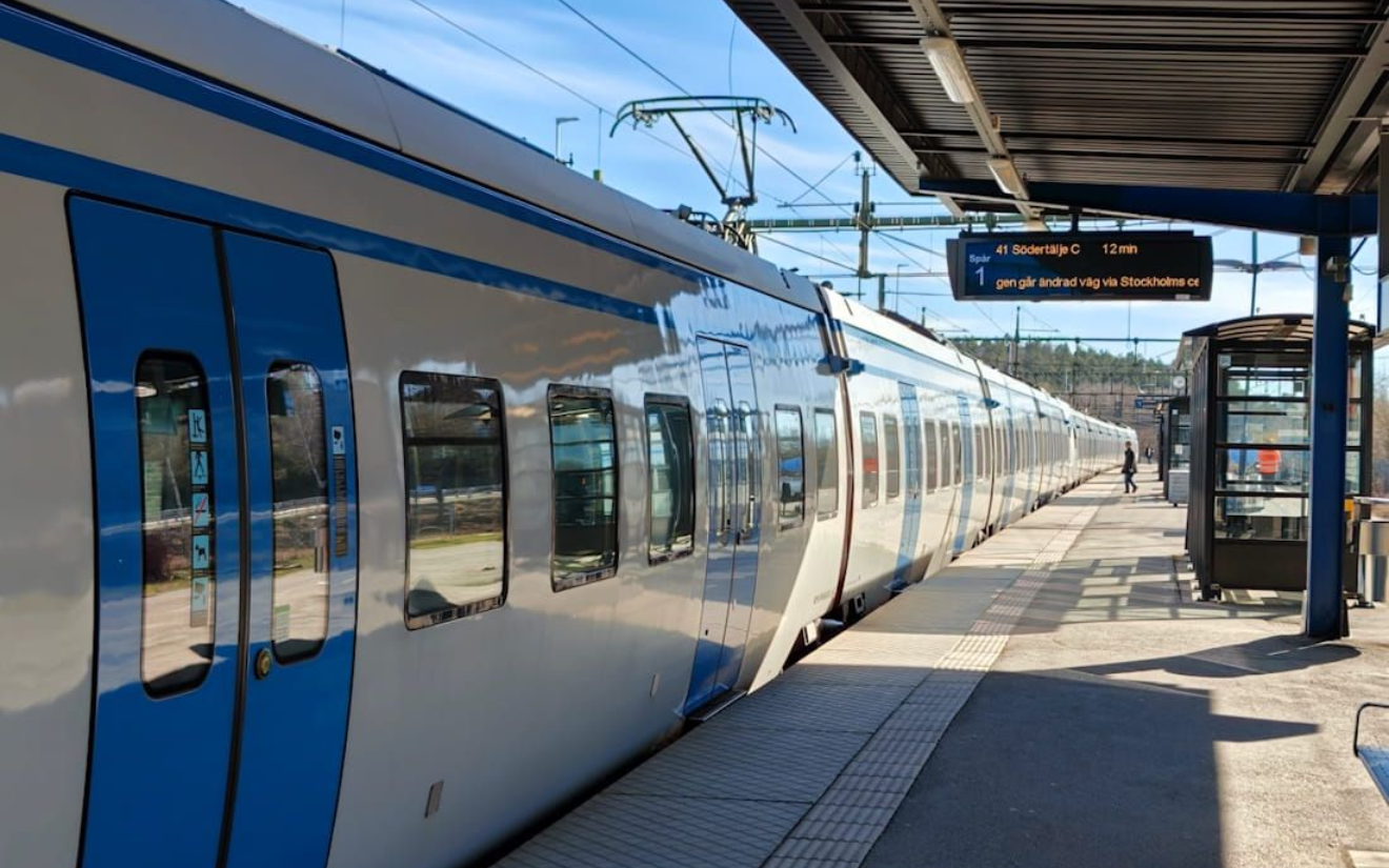 Stockholm Bahnhof Blue and white train stopped at a sunny station platform under a covered roof. Stockholm Bahnhof