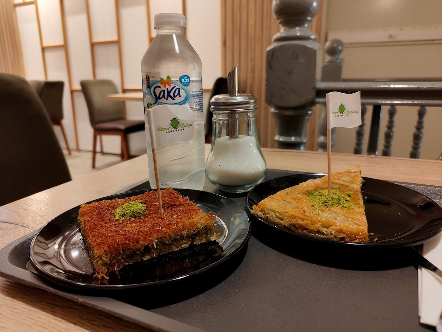 Two plated desserts on a café table with a water bottle and sugar shaker in the background