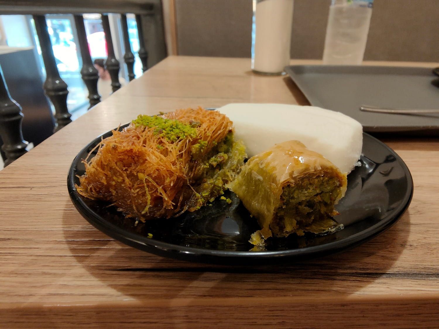 Two pastries on a black plate at a café table, one topped with green garnish and syrup and one wrapped in white paper.
