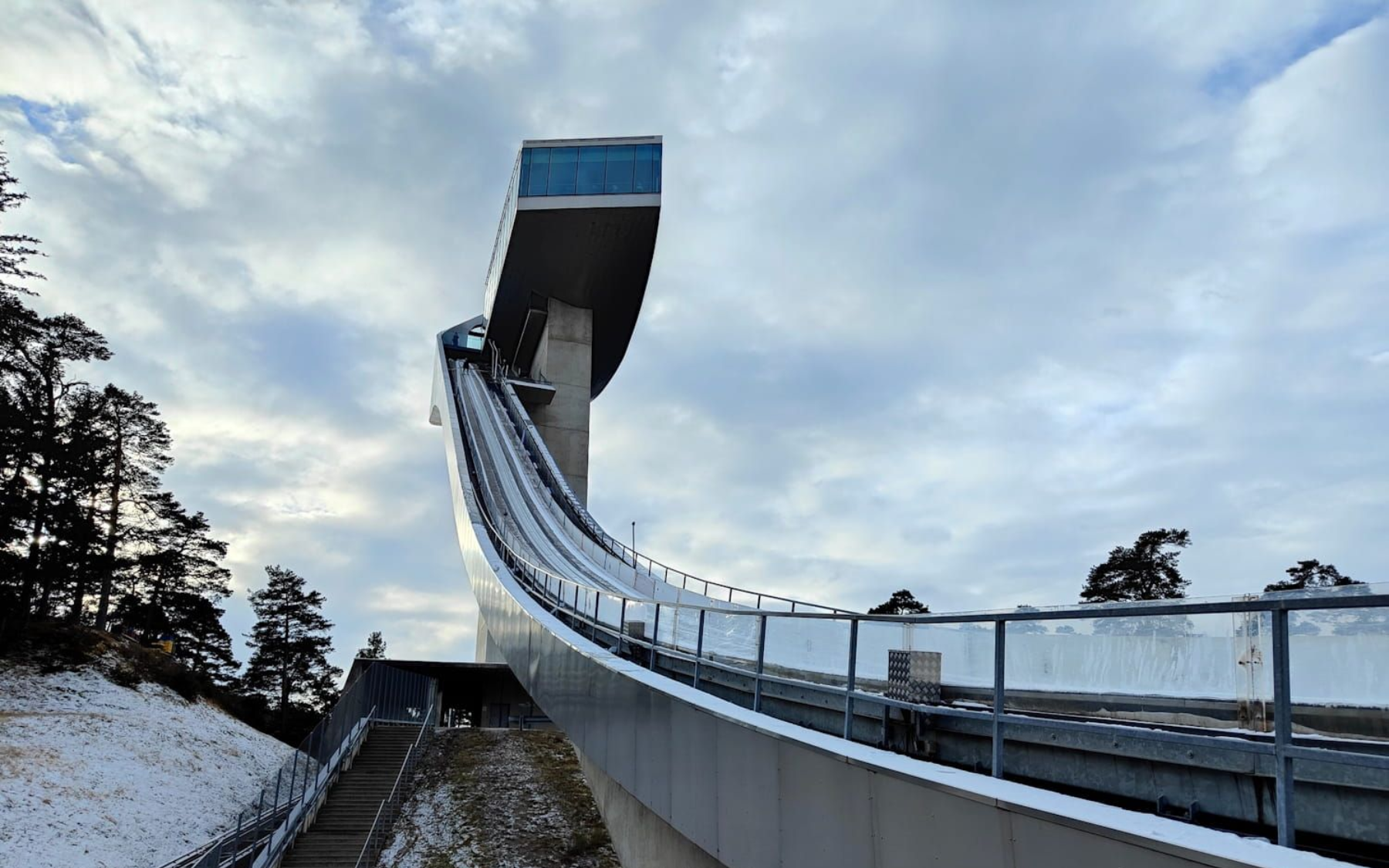 Bergisel Innsbruck Ski jump ramp in winter, leading to a high tower platform, with cloudy sky.