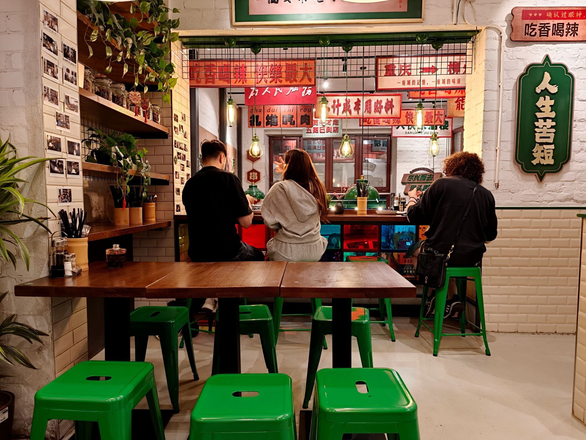 People seated at a small restaurant counter with green stools and warm red signage behind them