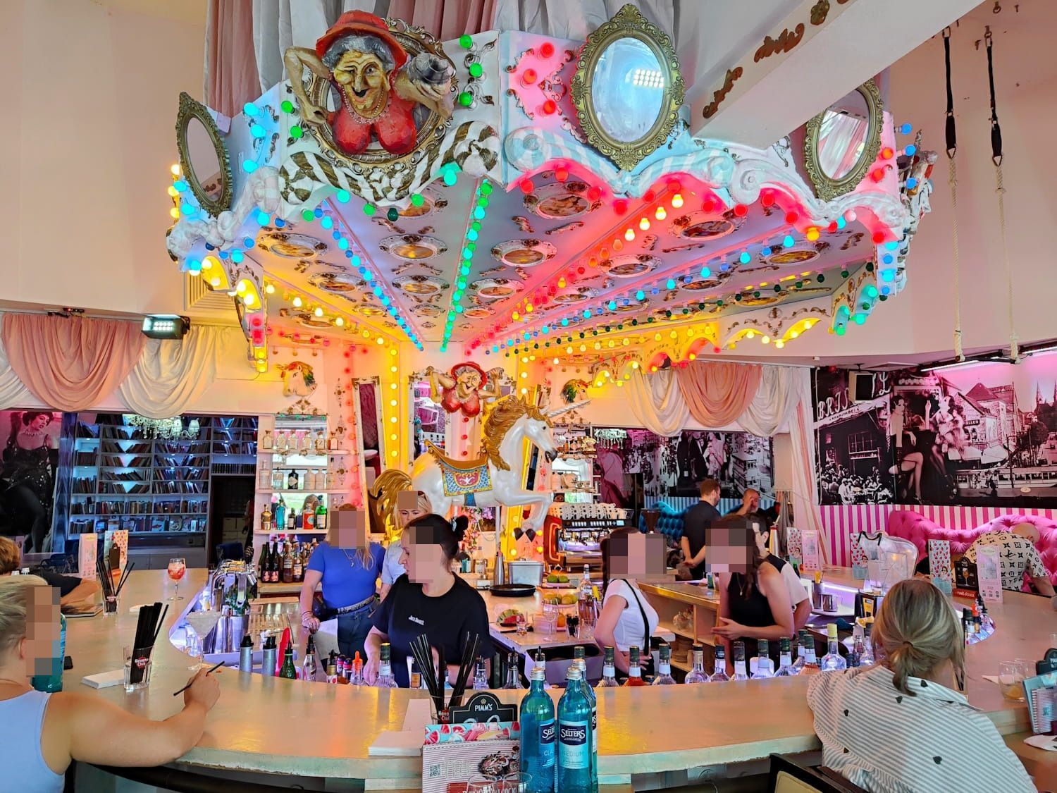 Wilde Matilde Colorful carnival ride indoors with people seated at a bar-like counter under bright neon lights