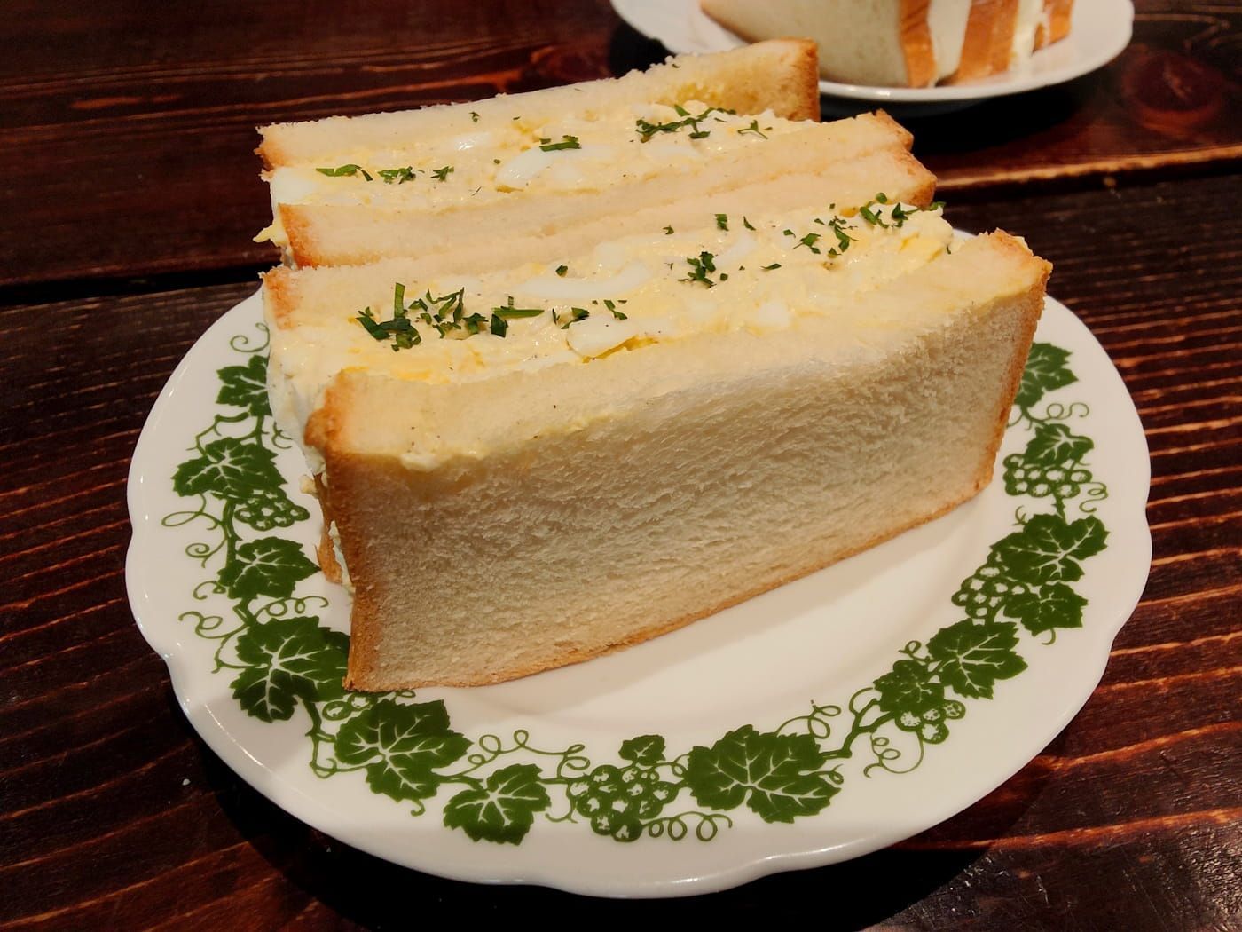 Three cucumber sandwich slices on a white plate with a green floral border