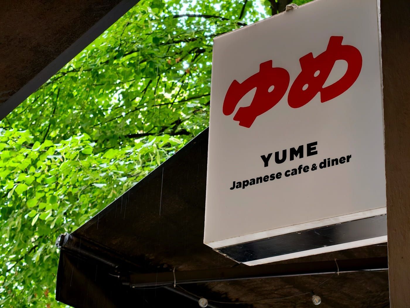 YUME Japanese café-diner sign with red lettering hanging under a green tree canopy