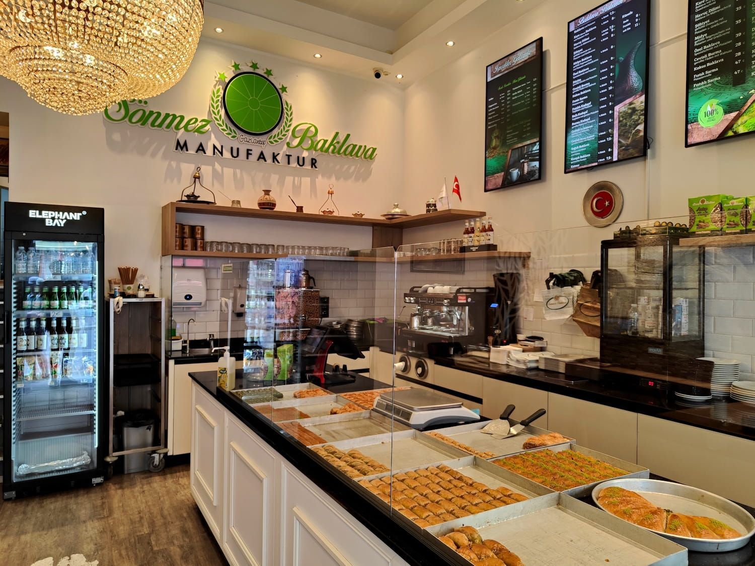 Berlin Kreuzberg Sönmez Bright deli counter with pastries, espresso machine, drink coolers, and menu boards in a modern cafe