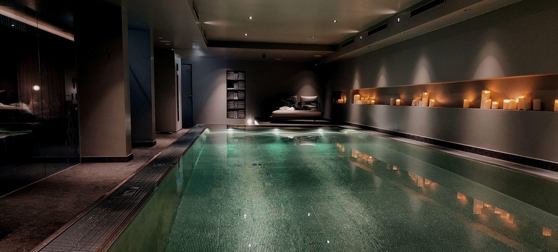 Hotel Das Innsbruck Pool Indoor spa with green-tiled pool, dark walls, ambient lighting, and candles along the wall.