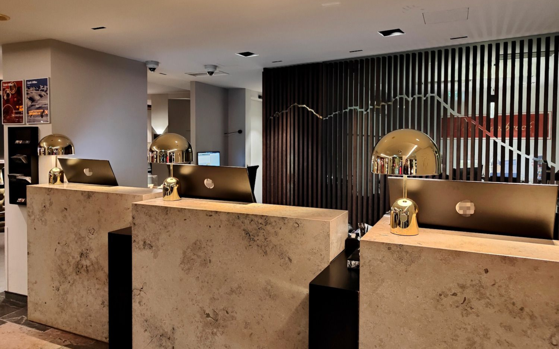 Das Innsbruck Rezeption Hotel reception area with three stone-like counters. Dark wood panel backdrop, gold accents, and warm lighting.