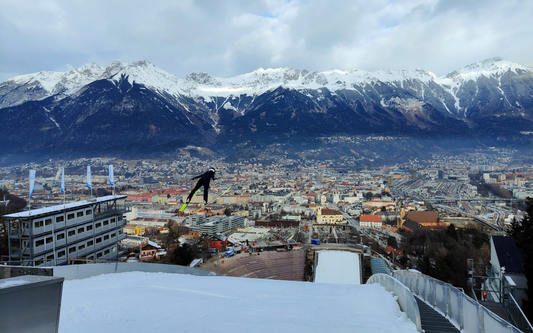 Die Bergisel Sprungschanze in Innsbruck Ski jumper in mid-air above Innsbruck, Austria, with snowy mountains in the background.