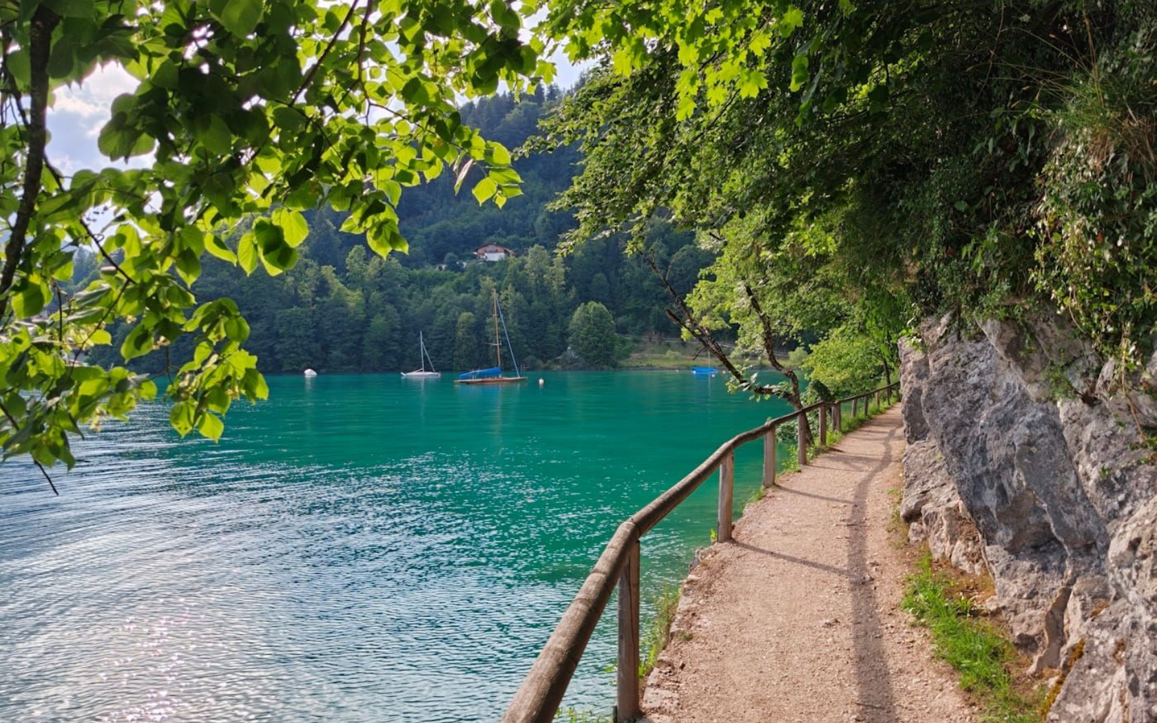 Fürbergweg Shaded lakeside path beside turquoise water and rocky shoreline, with trees overhanging the trail