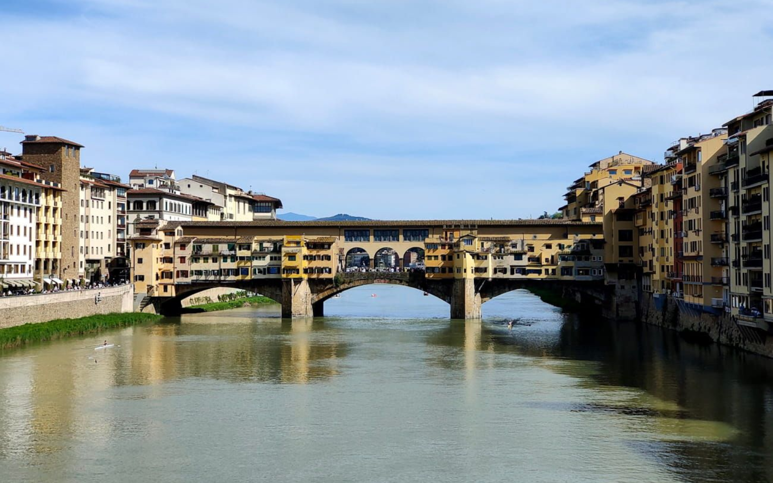Ponte Vecchio The Ponte Vecchio stone arch bridge with shops spanning the Arno River in Florence, Italy, under a blue sky.