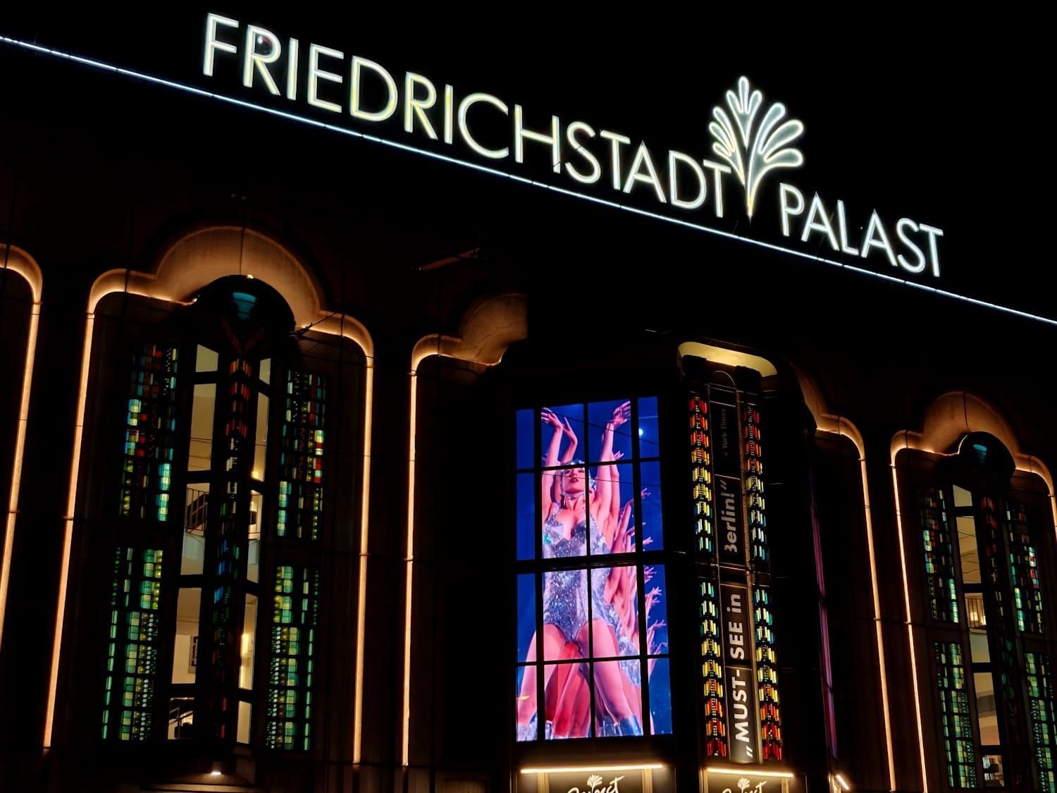 Illuminated Friedrichstadt-Palast theater facade at night, with colorful stage lights and a glowing sign.