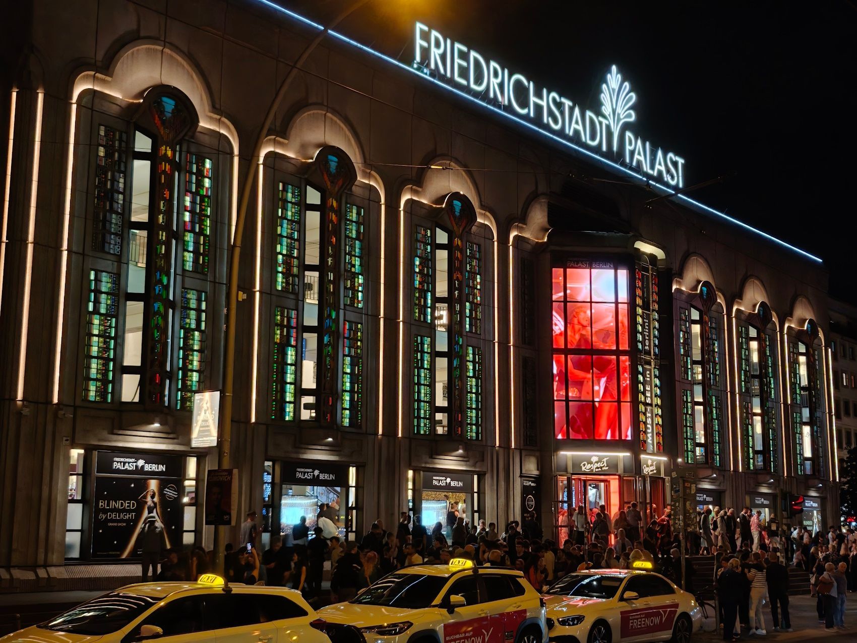 Night view of Friedrichstadt-Palast with glowing red windows and taxis lined up outside