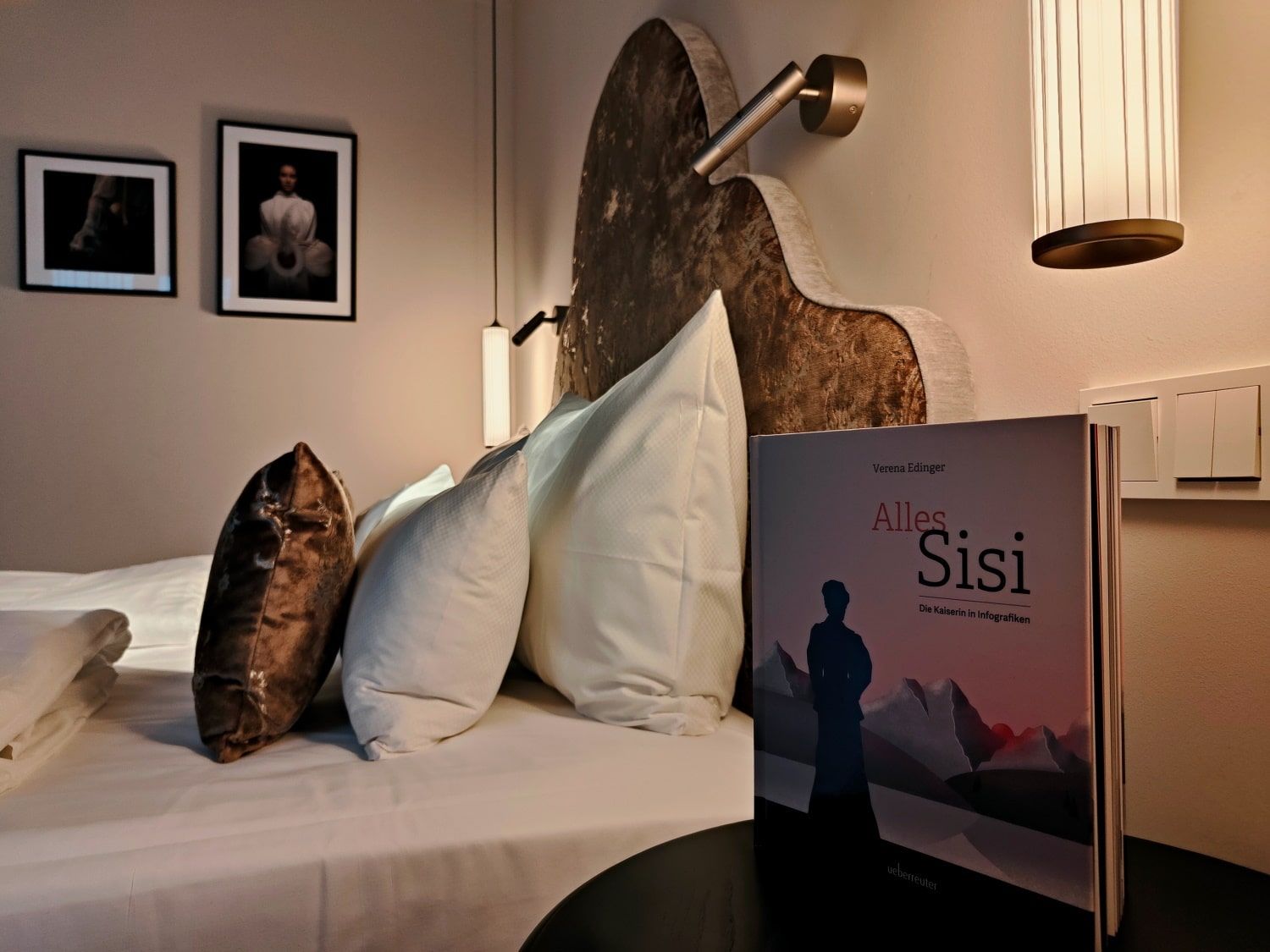 Bed with pillows, two framed portraits, and a book titled 
