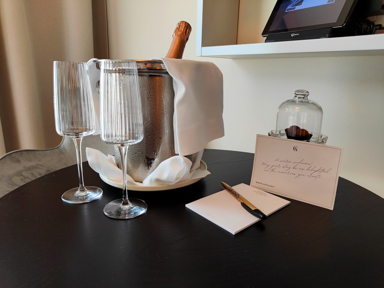 Two champagne flutes, ice bucket with bottle, card, pen on table.