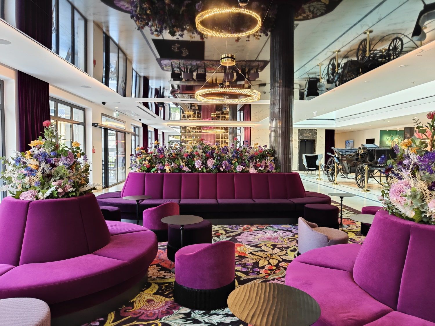 Grand Elisabeth Hotel Lobby A vibrant hotel lobby with purple seating, floral arrangements, mirrored ceiling, and circular chandeliers.