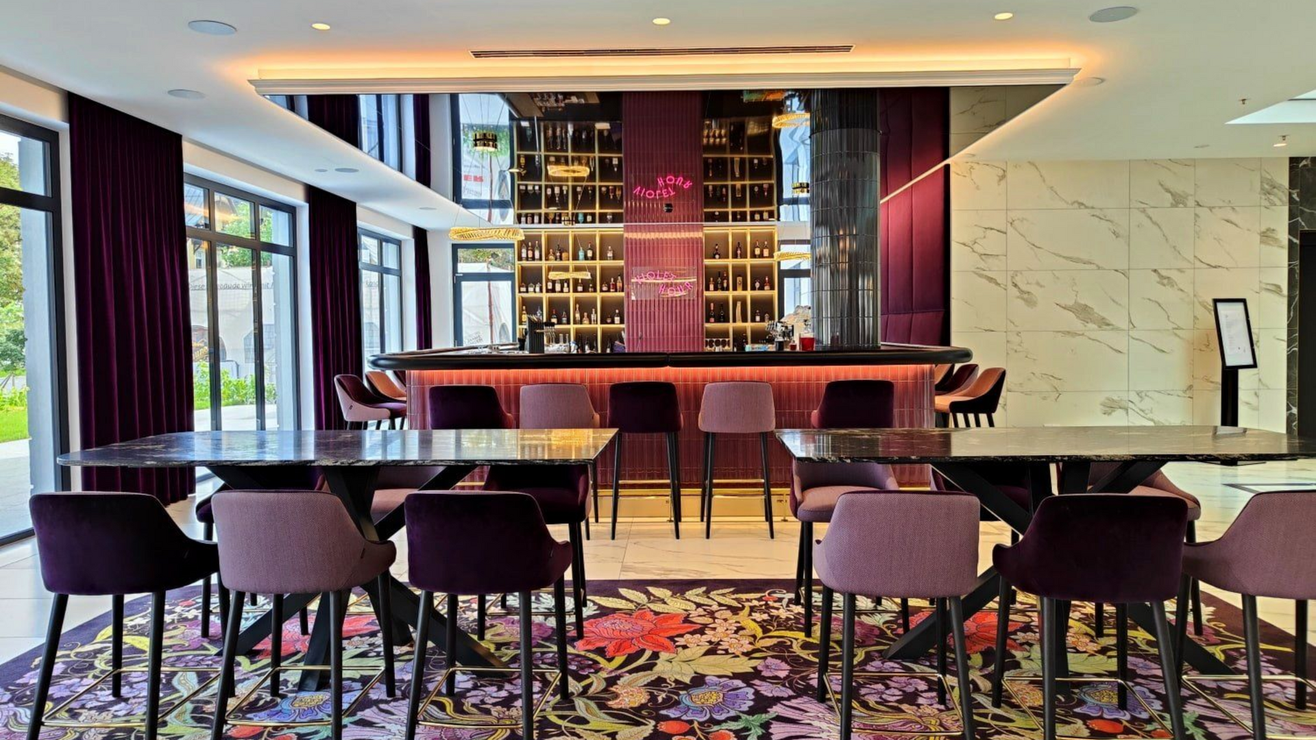 Hotel Grand Elisabeth Luxurious bar interior with a floral rug, purple accents, and dark tables.
