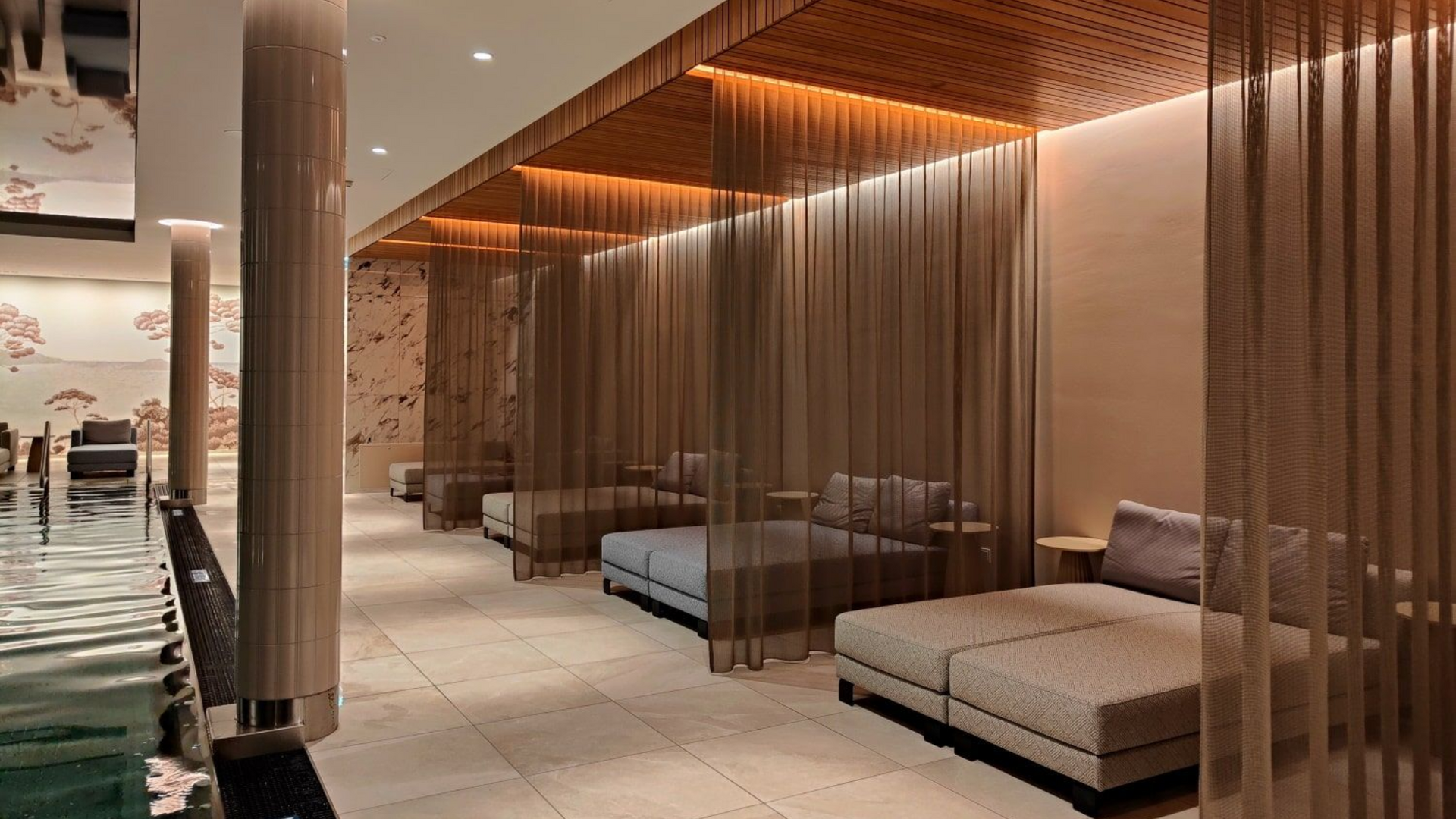 Grand Elisabeth Hotel Wellness Spa lounge with daybeds separated by hanging metal curtains next to a pool.