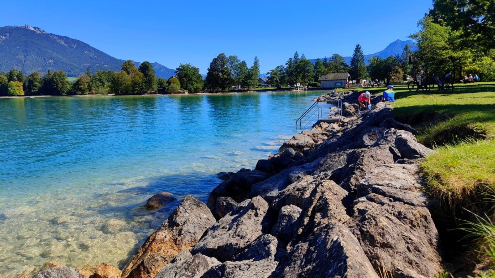 Wolfgangsee Rocky shoreline with turquoise water, mountains, and a clear blue sky.