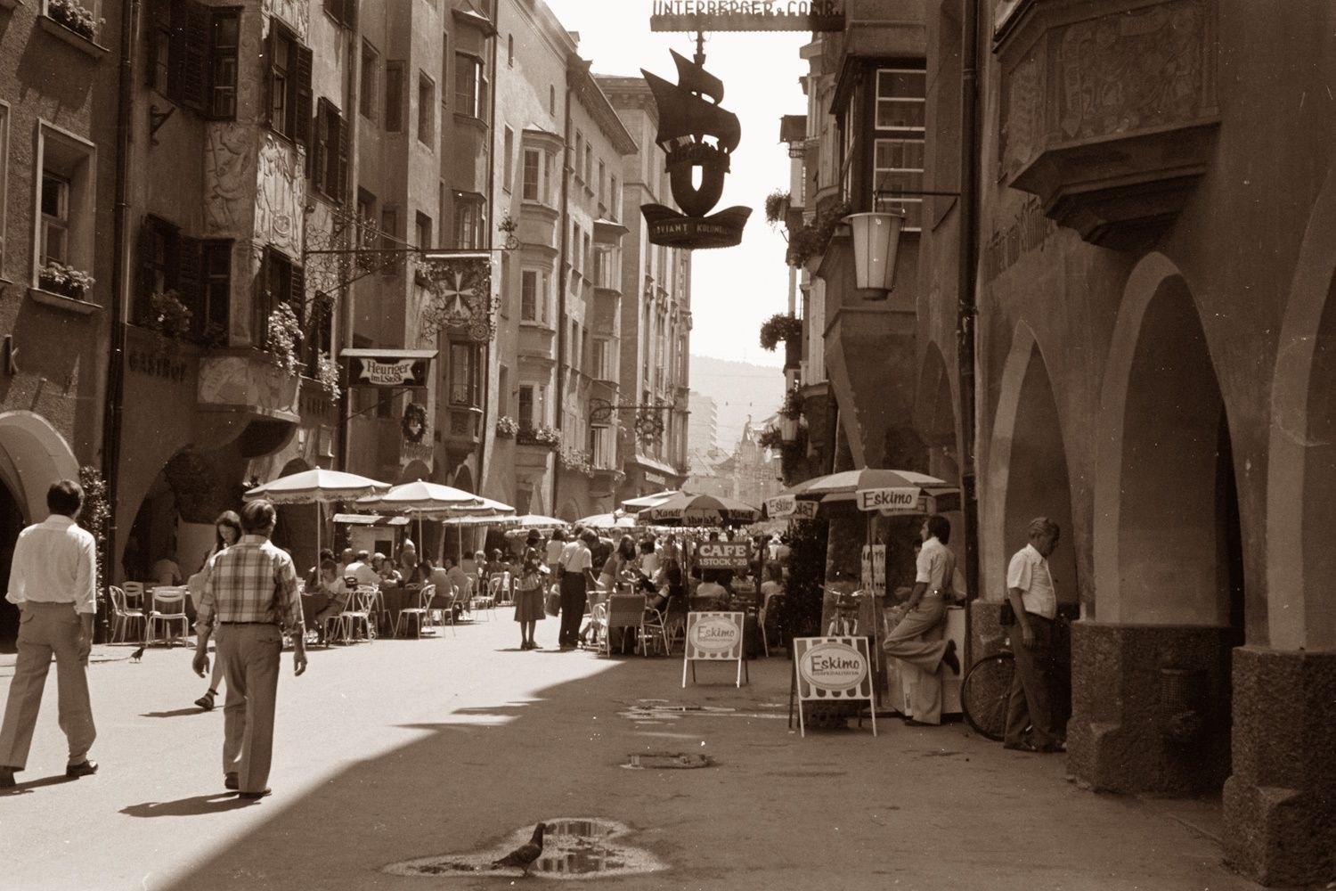 Street scene with shops, people, and arched walkways in a European town.