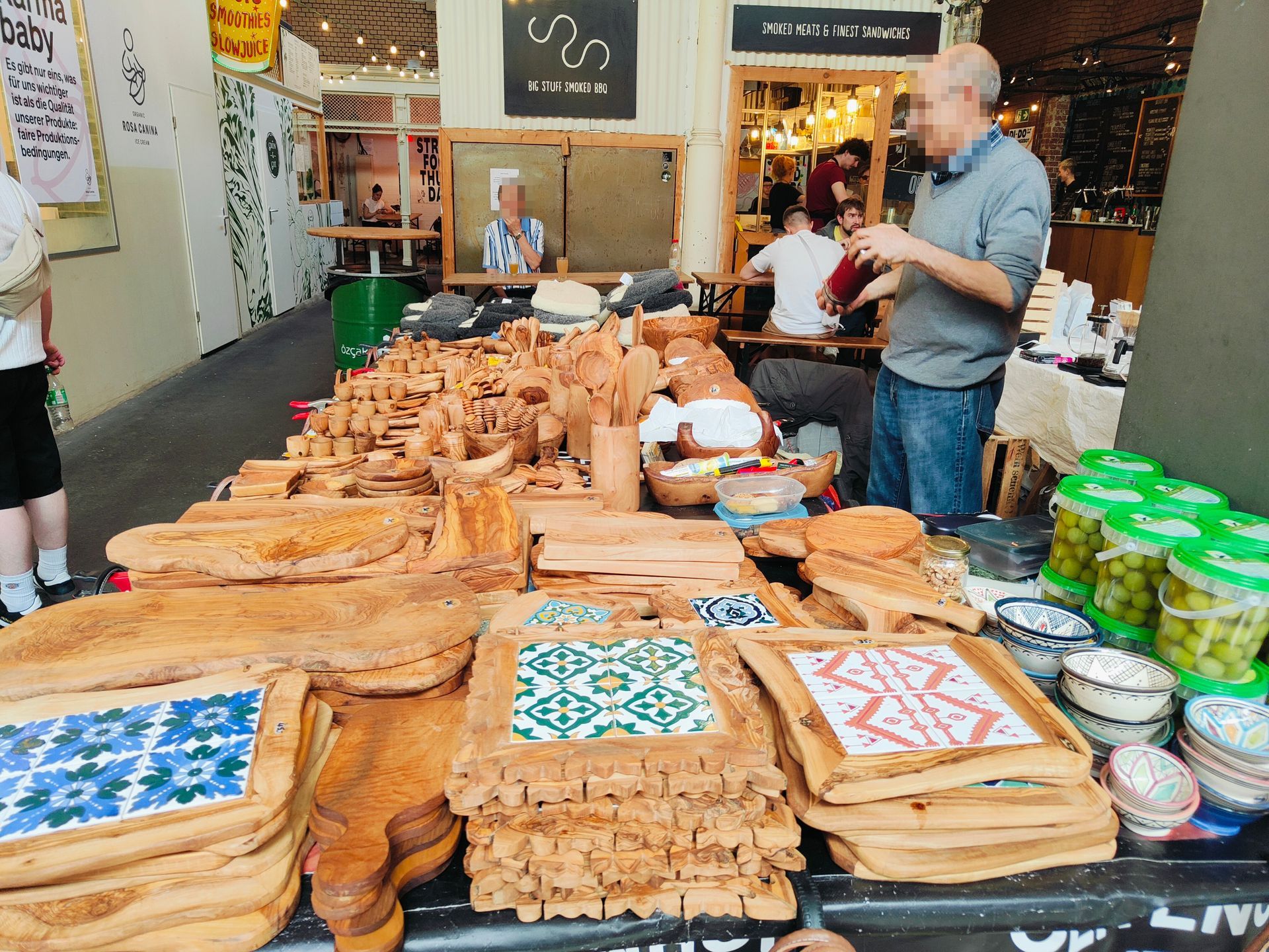 Market stall with trays of pastries and jars of sweets, with a vendor standing behind the display.