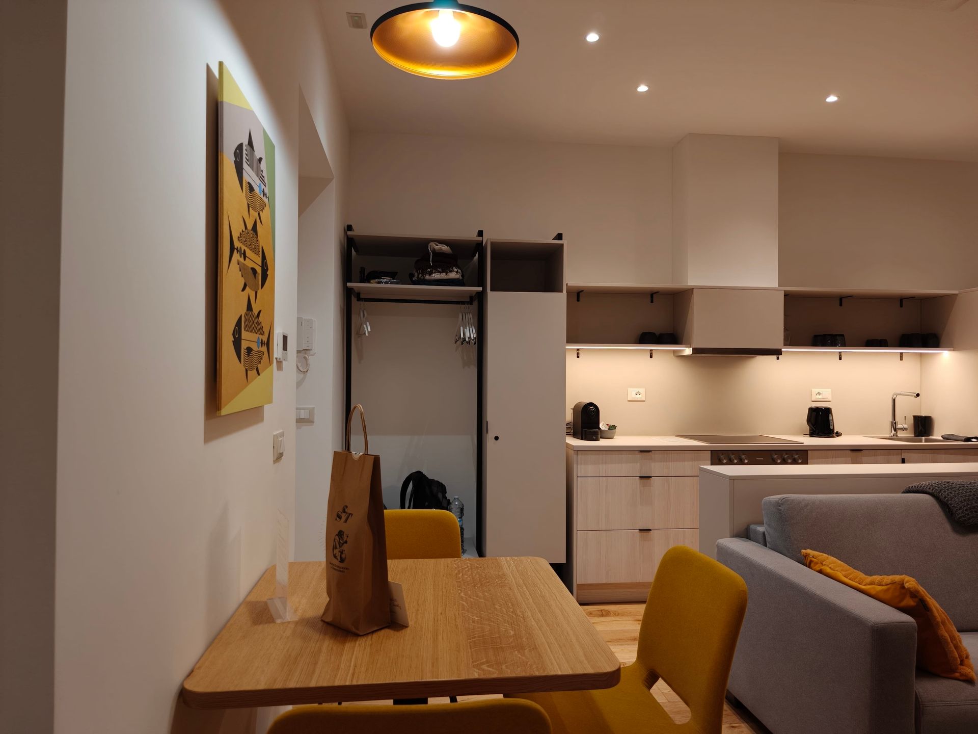 Urbanauts Modern kitchen-living room with wood table, gray sofa, and warm overhead lighting