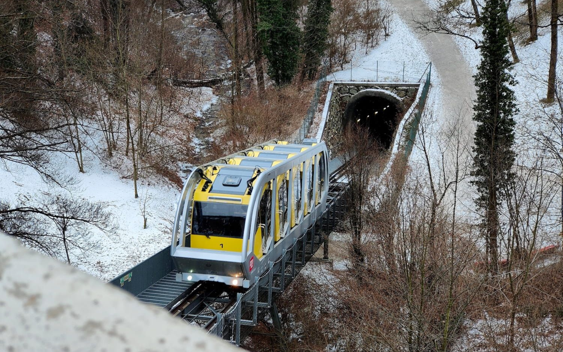 Innsbruck Nordkettenbahnen Yellow funicular train on tracks near snow-covered trees and a tunnel entrance.