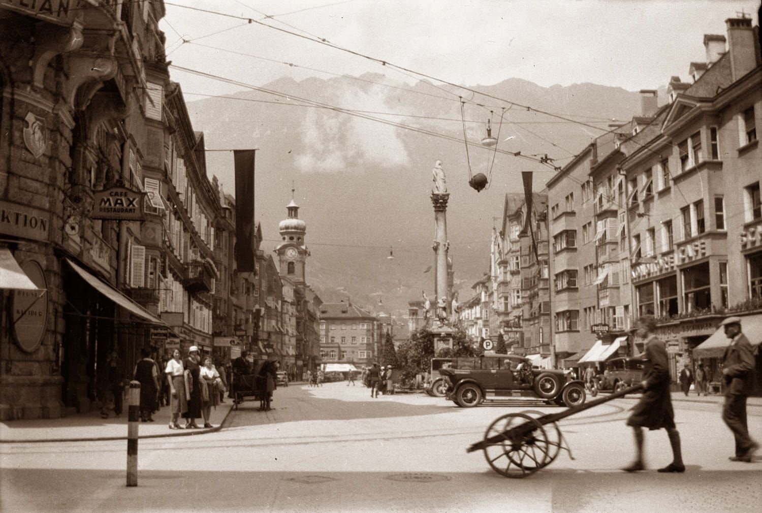 Street scene in Innsbruck, Austria with buildings, vehicles, people, and mountains in the background.