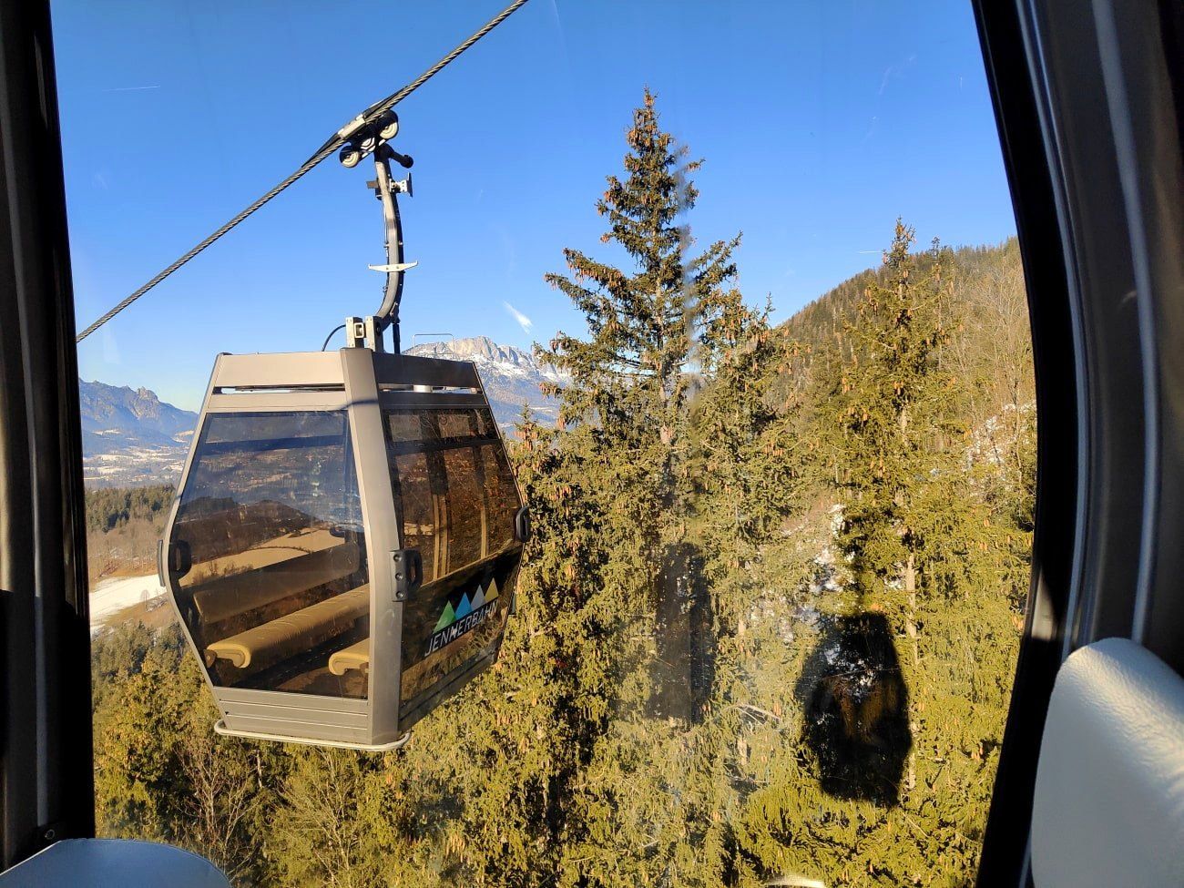 Jennerbahn Gondel A cable car going up a mountain with trees in the background