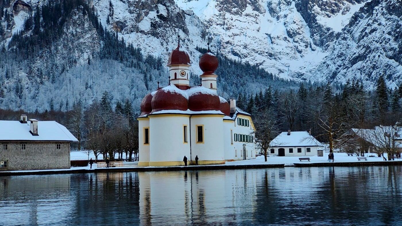 Wallfahrtskirche St. Bartholomä A small church sits in the middle of a lake surrounded by snow covered mountains