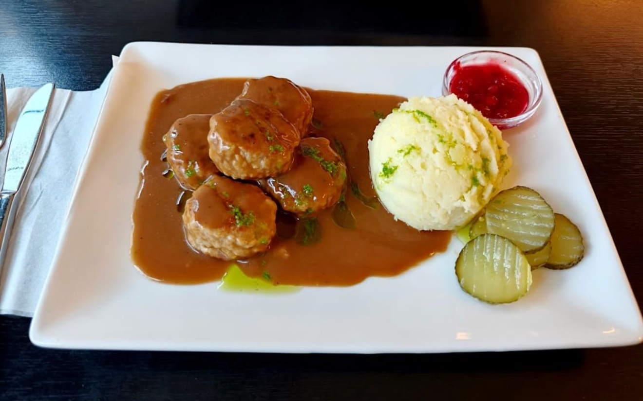 Plated meatballs with brown gravy, mashed potatoes, pickles, and cranberry sauce on a white plate