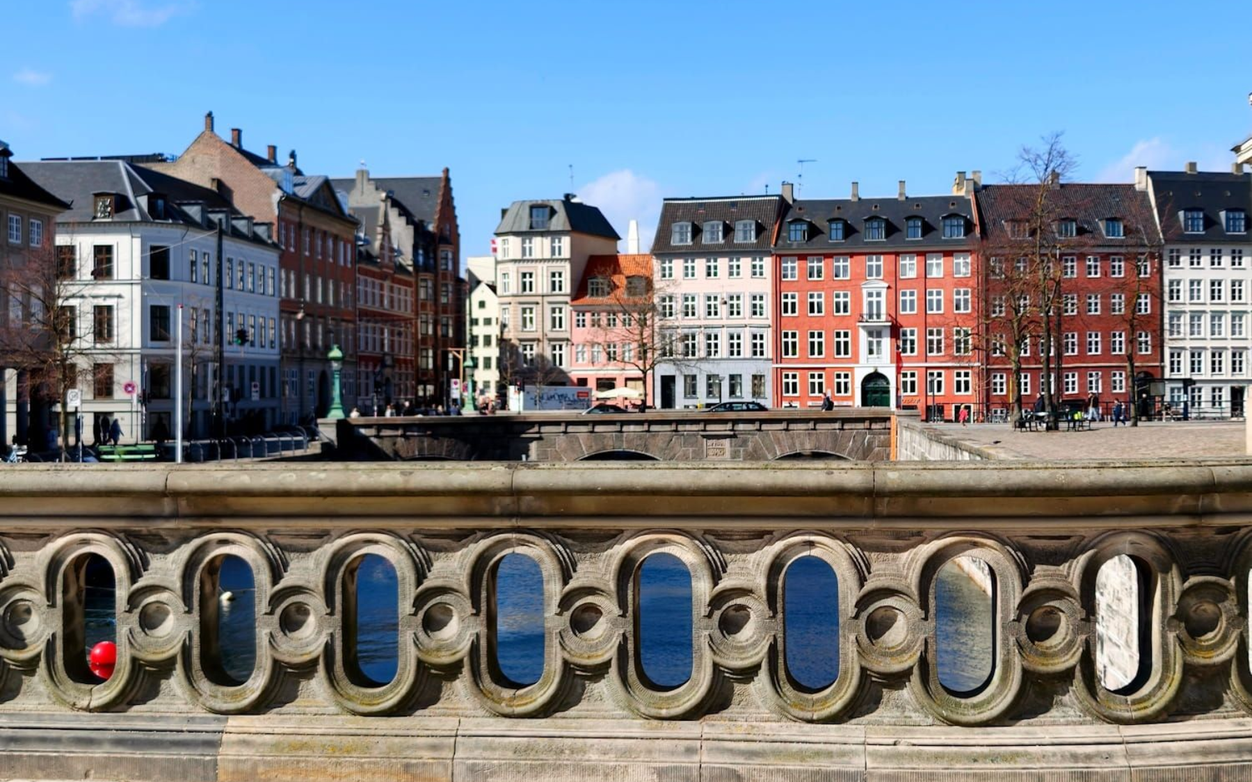 Kopenhagen Colorful waterfront buildings across a river, viewed over a stone balustrade under a blue sky